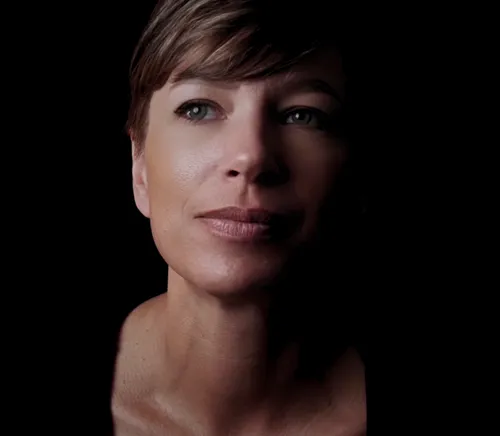 Close-up portrait of a woman with short hair looking slightly up and to the side against a black background.