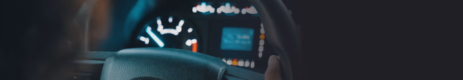 Close-up of a Omni car dashboard showing speedometer and a hand on the steering wheel.
