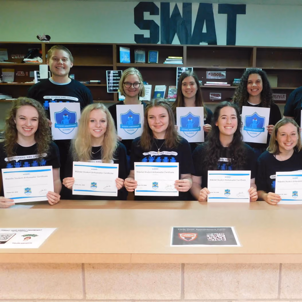 Group of students smiling and holding Wakelet Student Ambassador Certificates in front of shelves and SWAT sign.