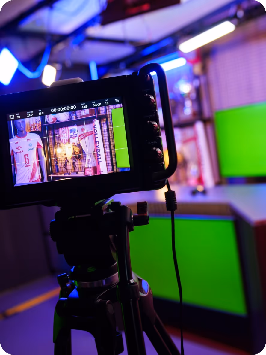 Kamera na statywie nagrywająca scenkę sportową z manekinami i sprzętem do siatkówki w studiu z zielonymi ekranami.