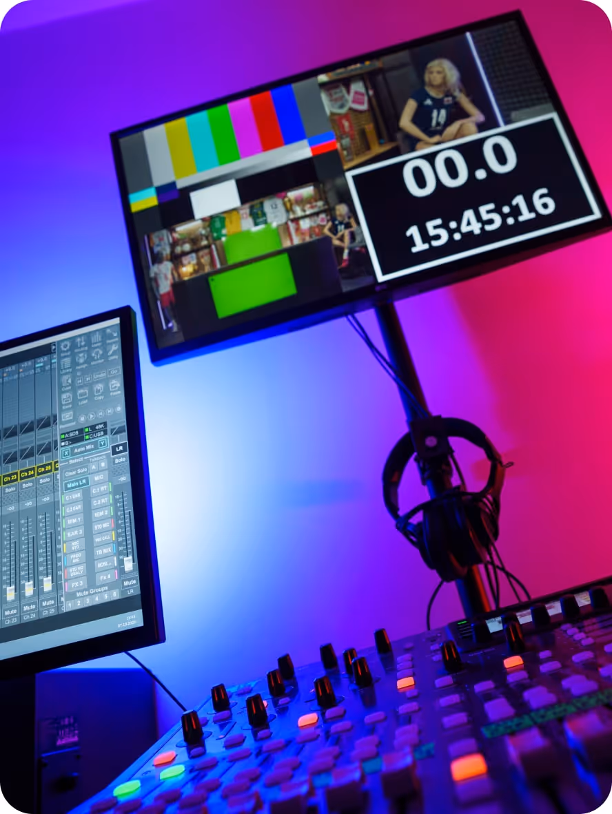 Sala kontroli transmisji z konsoletą miksującą dźwięk i dwoma monitorami, na jednym wyświetlają się paski kolorów, licznik czasu i obraz wideo.