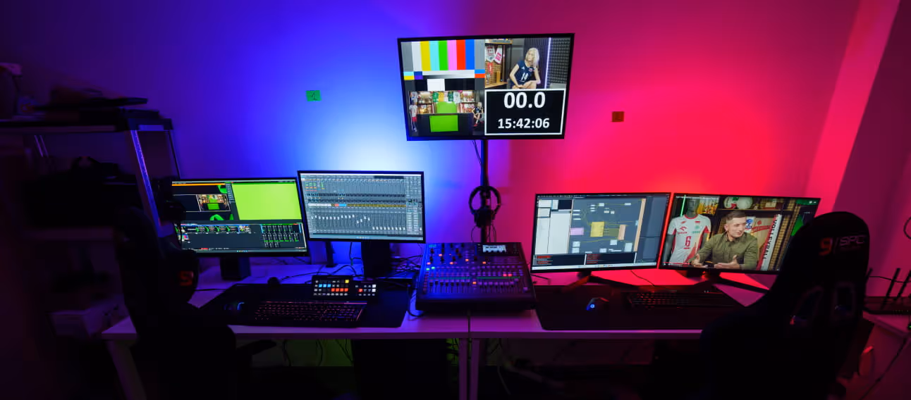 Sala kontroli transmisji z wieloma monitorami, na których wyświetlane jest oprogramowanie do edycji wideo oraz obraz na żywo, oświetlonymi niebieskim i różowym światłem.