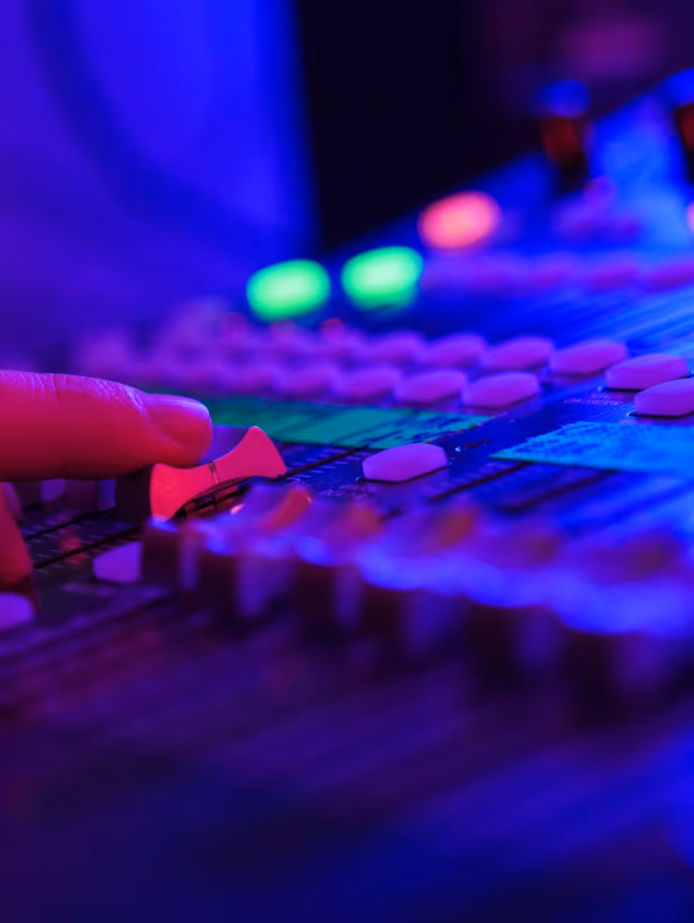 Palcem przesuwasz suwak na konsoli miksującej dźwięk z kolorowymi diodami LED w odcieniach niebieskiego i fioletu.