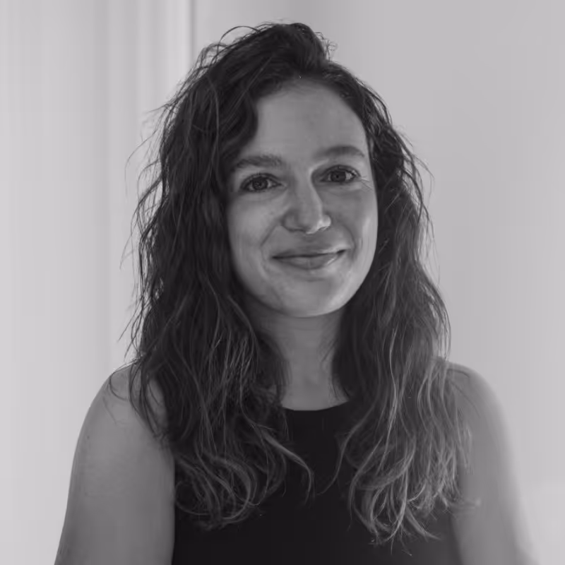 Retrato en blanco y negro de mujer con cabello rizado y suelto, sonriendo levemente, con camiseta sin mangas negra.