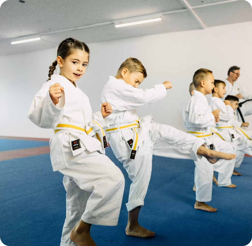 Children practicing karate in white uniforms with yellow belts on a blue mat in a dojo.