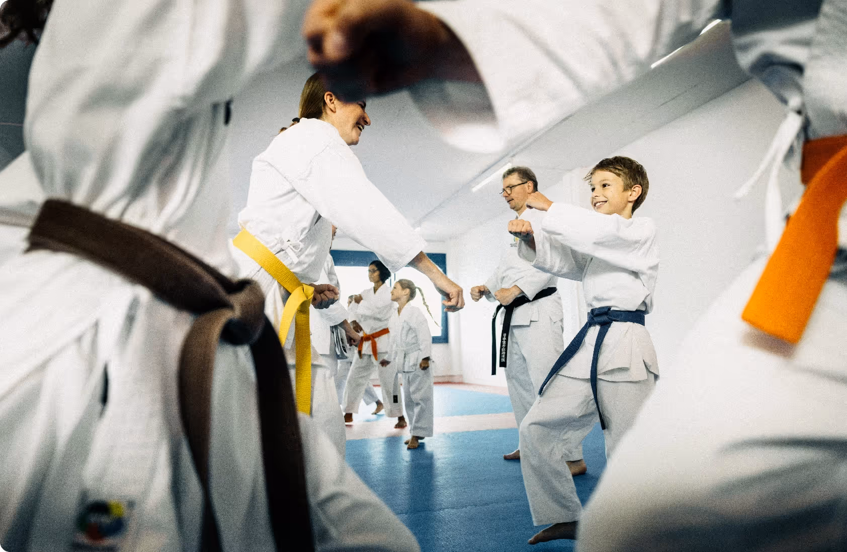 Children and adults practicing karate punches in a dojo, wearing white uniforms with various colored belts.