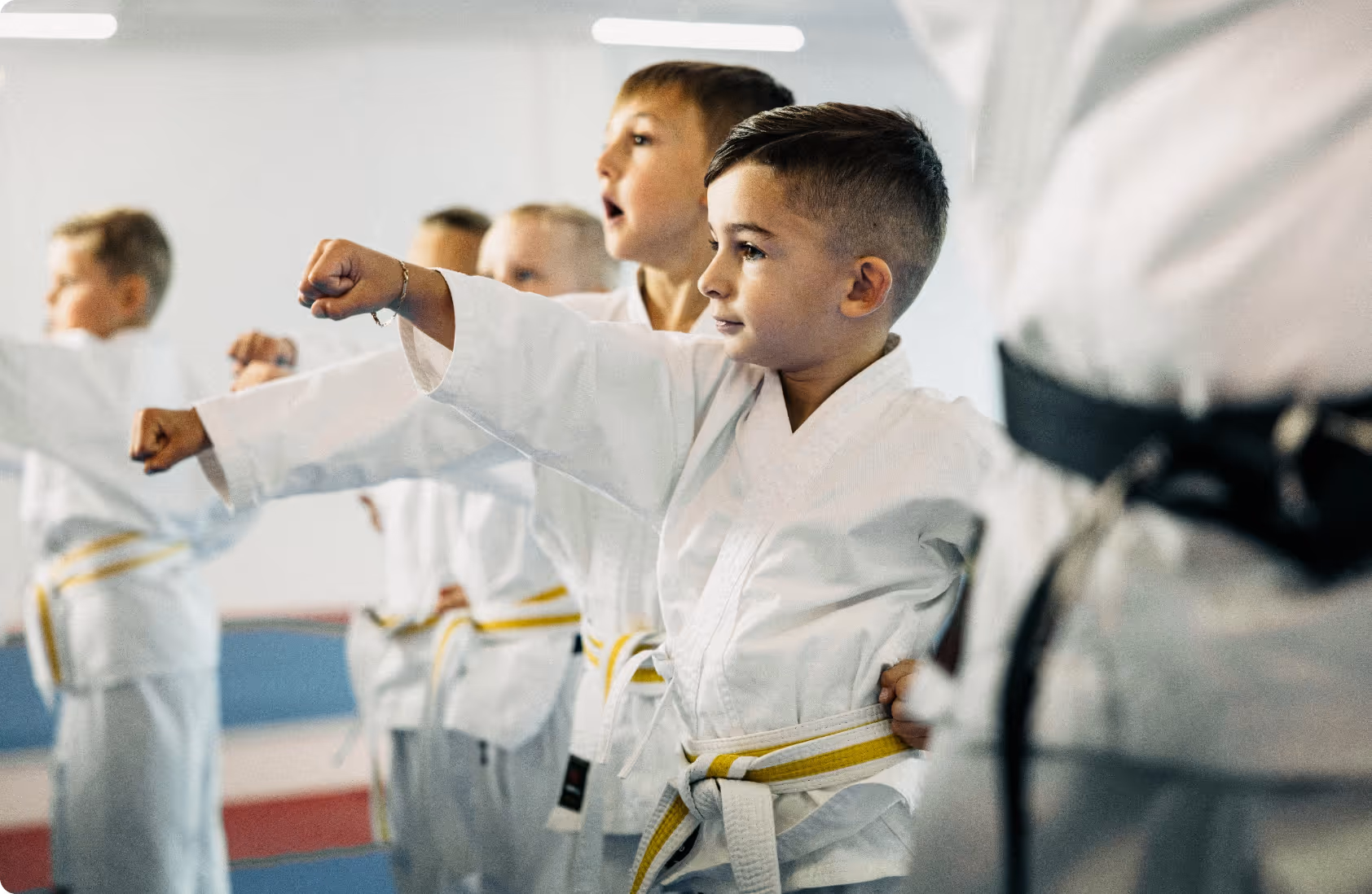 Young boys in white karate uniforms with yellow belts practicing a punching technique in a dojo.