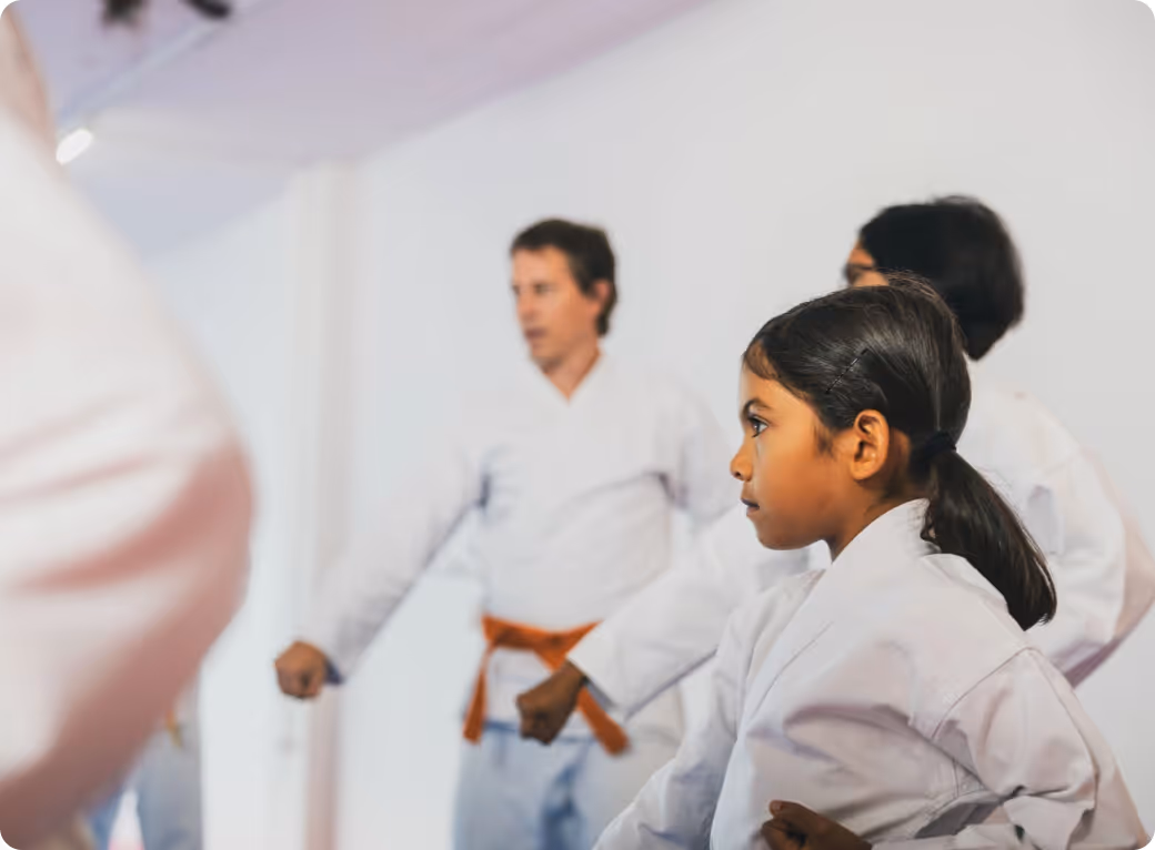 Young girl in a white karate uniform practicing a punch with others in the background.