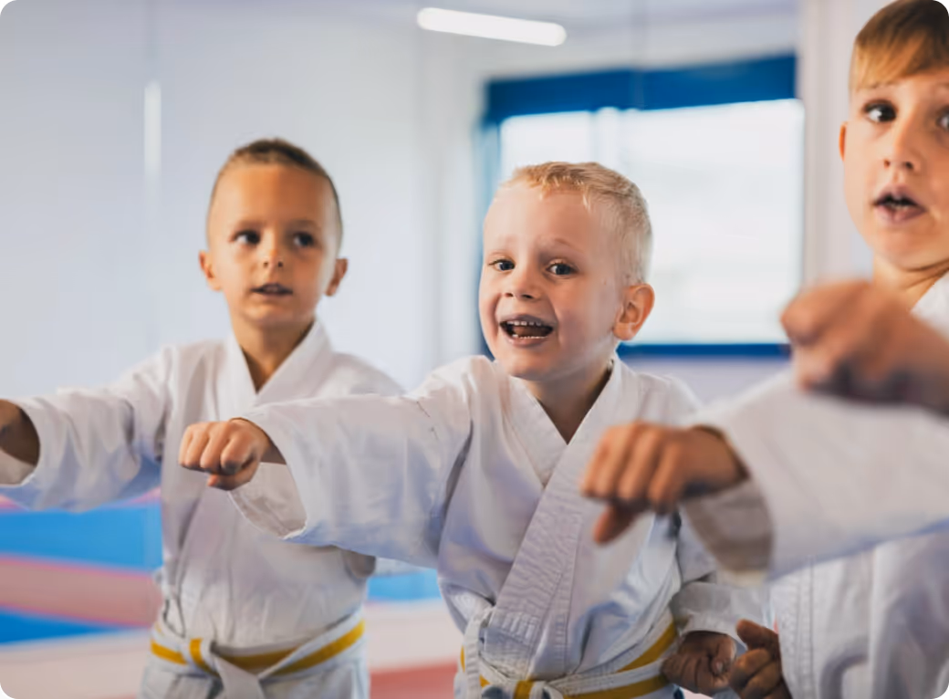 Three young boys in white martial arts uniforms with yellow belts practicing punches in a dojo.