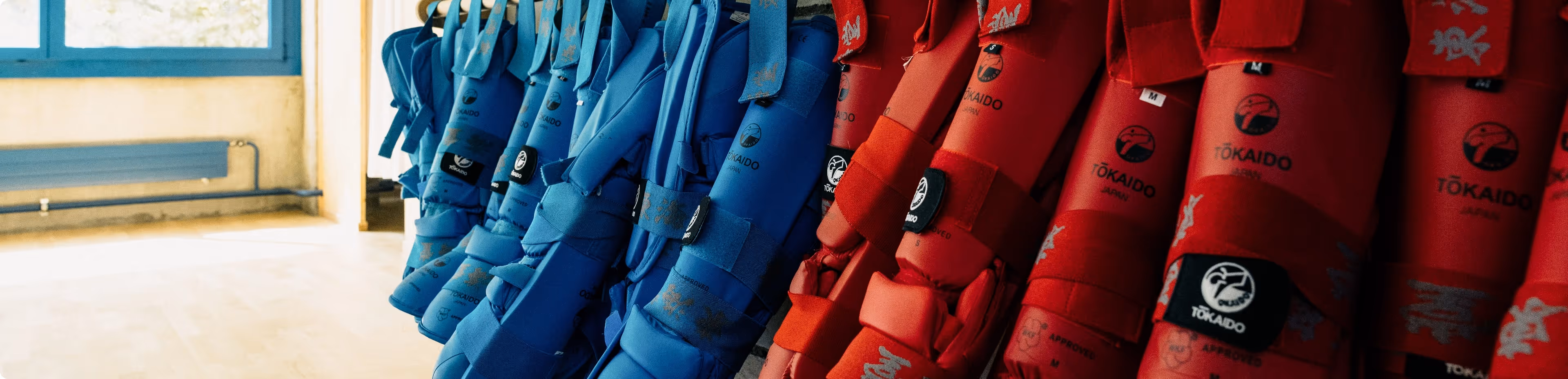 Rows of red and blue Tokaido karate body protectors hanging in a training room.