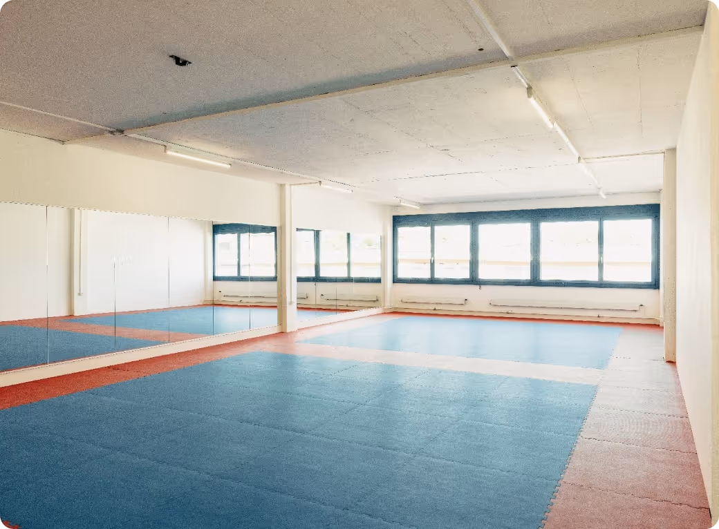 Empty martial arts training room with blue and red padded floor and mirrored wall.