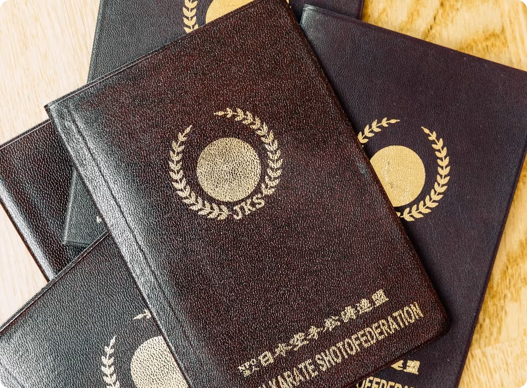 Stack of dark brown leather-bound booklets with gold emblem and Japanese text reading Karate Shotofederation.
