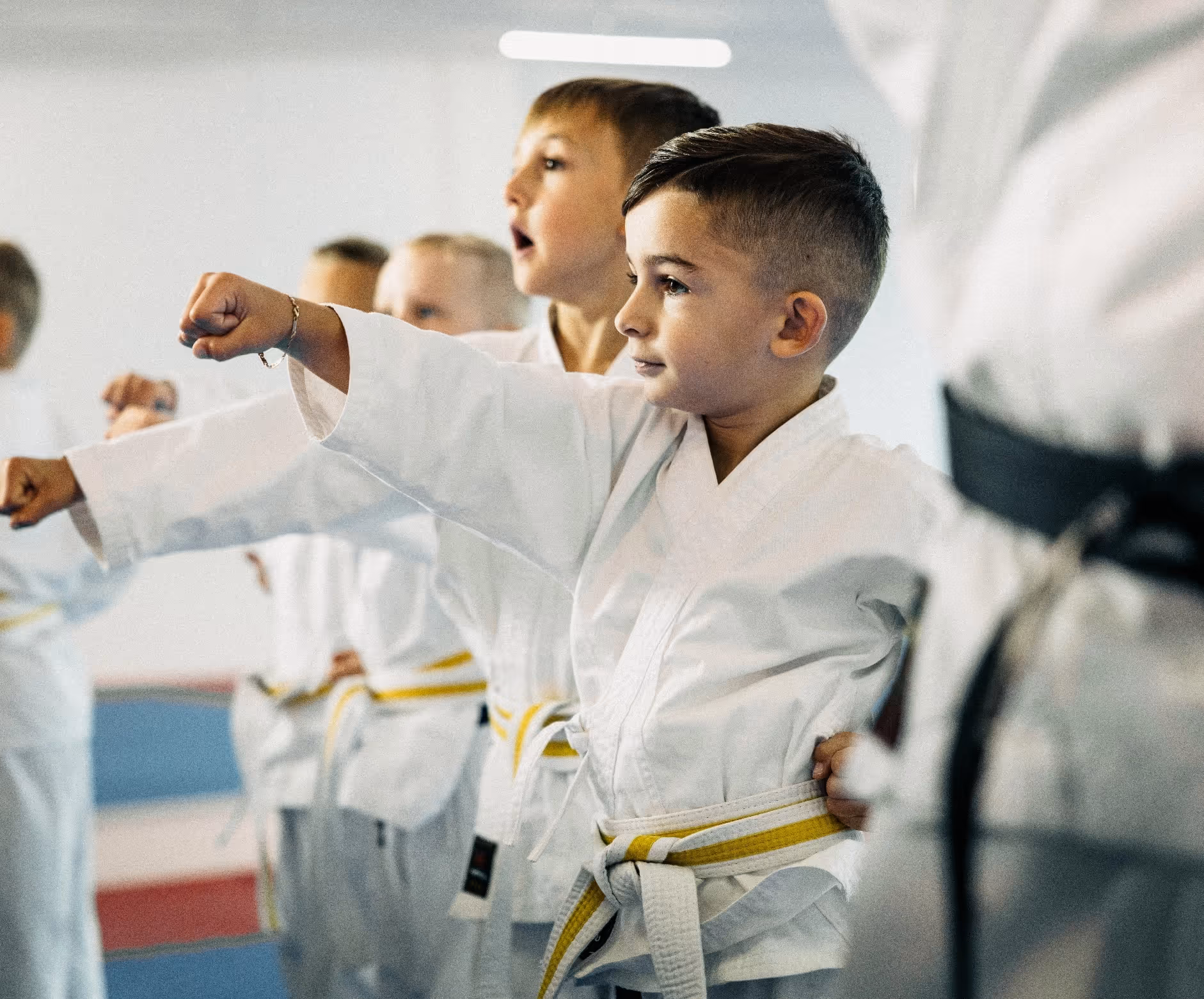 Young boys in white karate uniforms with yellow belts practicing punches in a martial arts class.