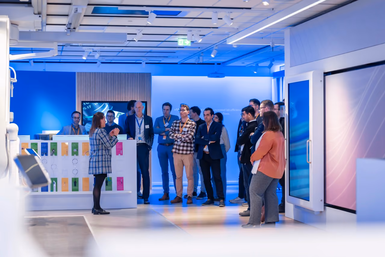 A woman presenting to a group of people in a modern tech showroom with digital displays.