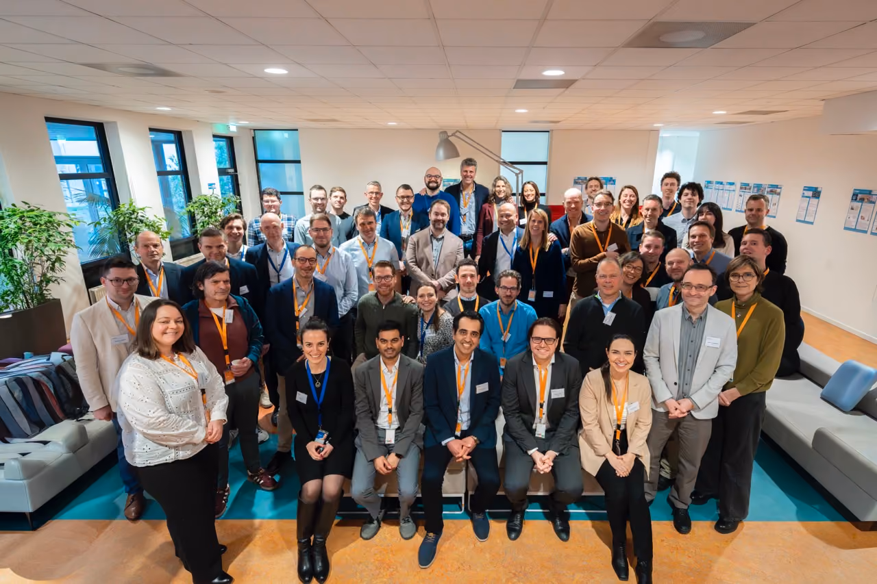 Large group of diverse professionals posing for a photo in a bright office space.