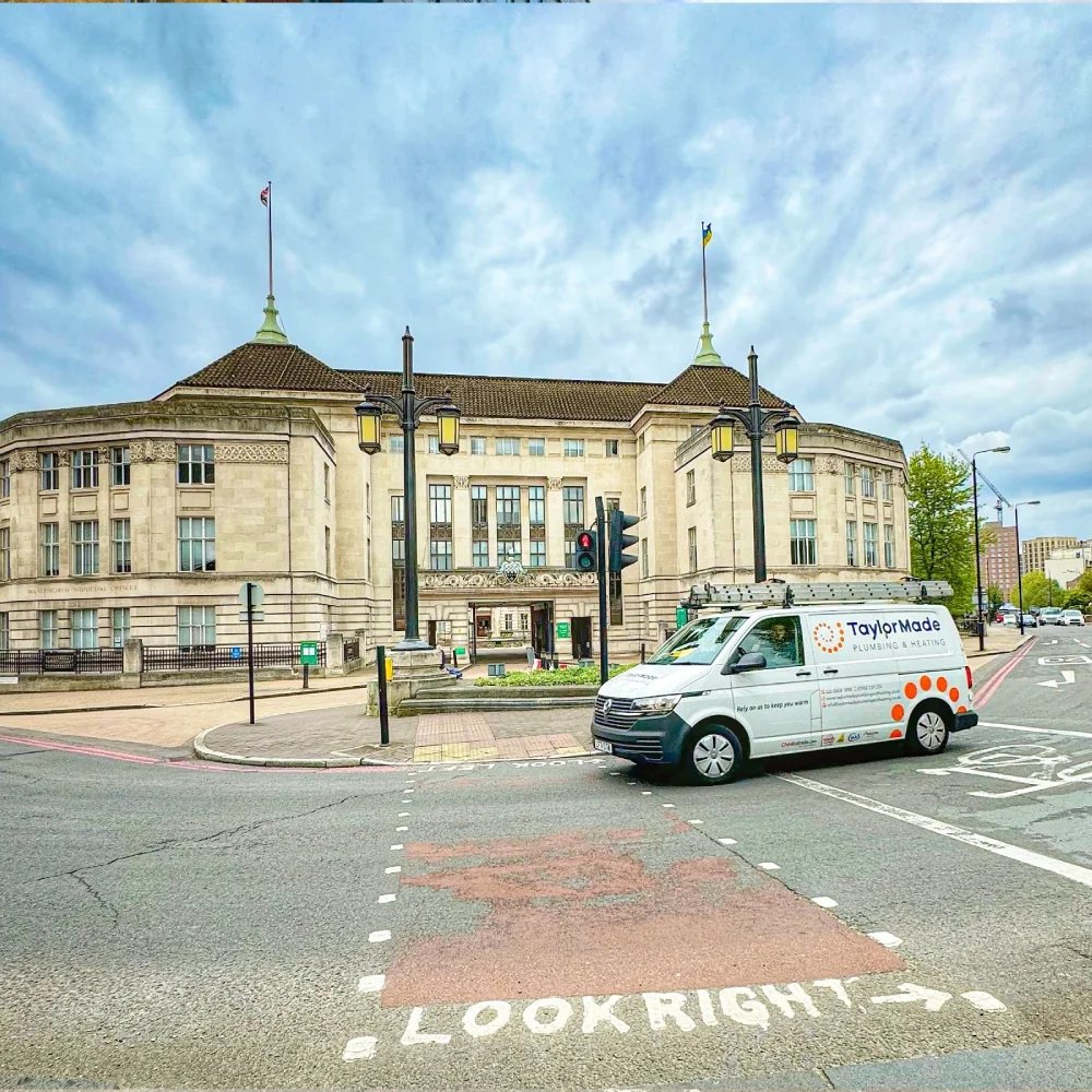 White TaylorMade plumbing van at crosswalk with 'LOOK RIGHT' painted on road near historic building.