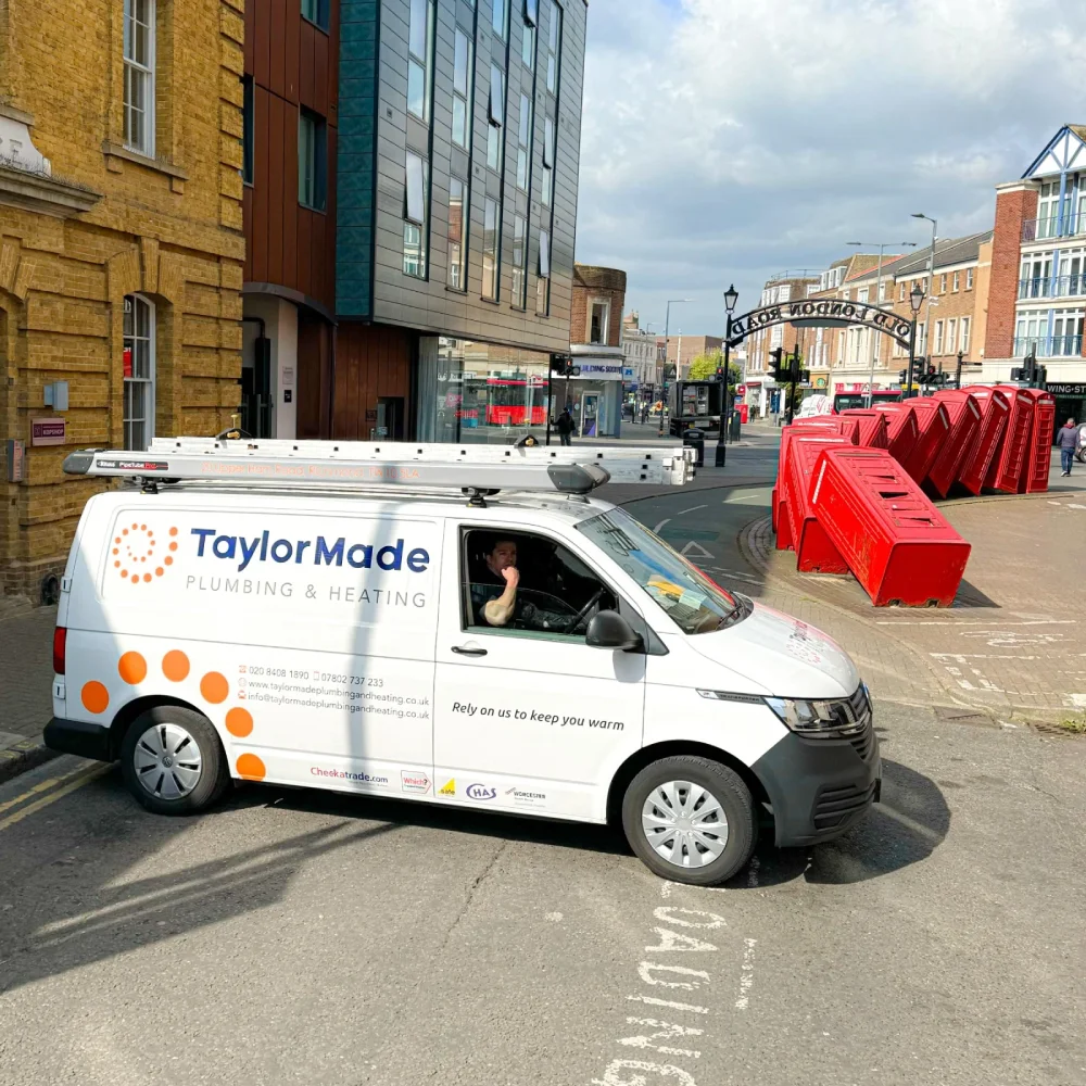 White Taylor Made Plumbing & Heating van parked on street with row of tilted red phone booths nearby.