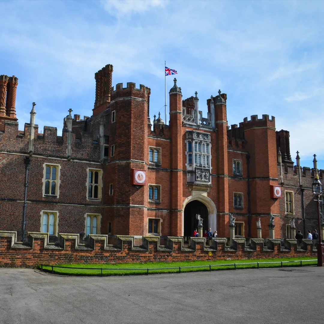 Historic brick castle with turrets, statues, and a Union Jack flag on a clear day.