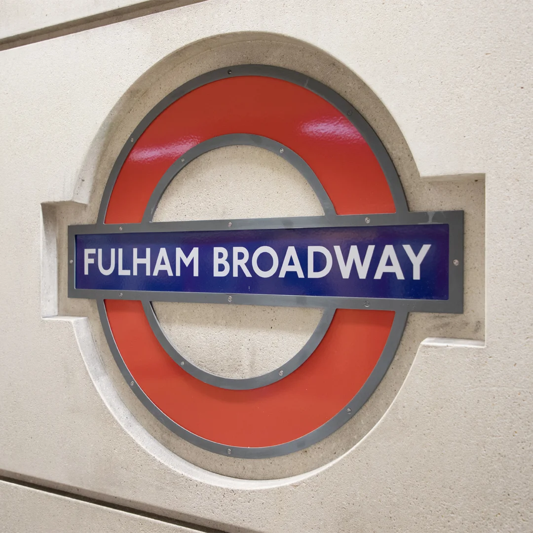 London Underground sign for Fulham Broadway station mounted on a beige wall.