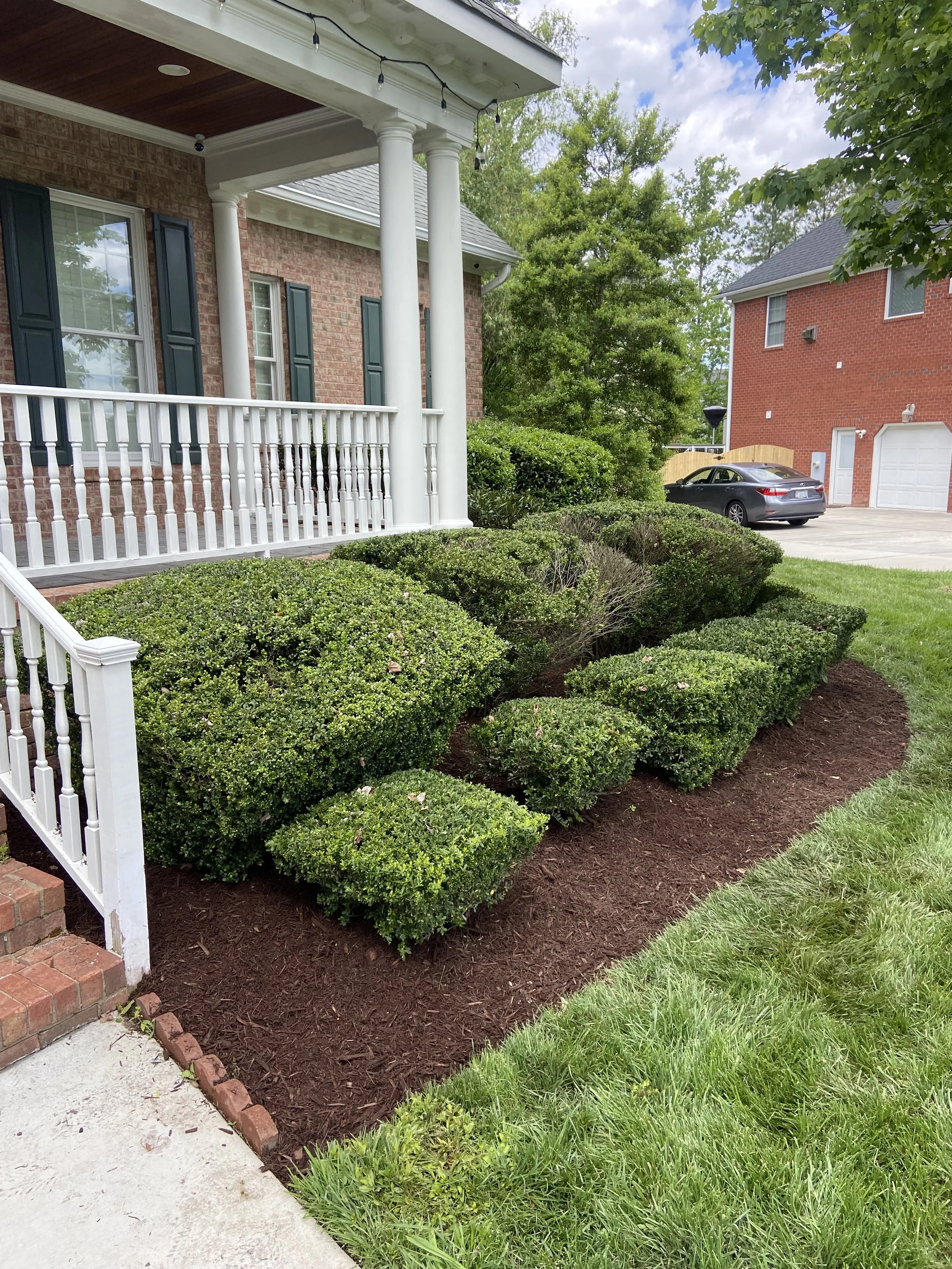 Trimmed hedges and fresh mulch beside a front porch