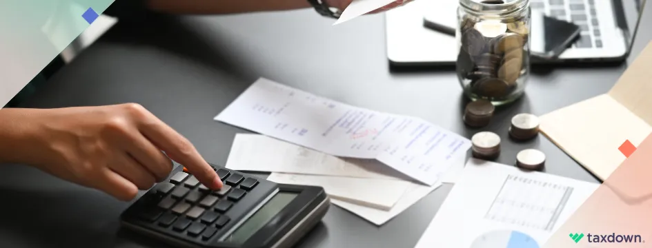 Persona calculando gastos con una calculadora, rodeada de facturas, monedas y documentos financieros