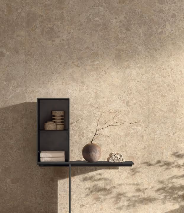 Moderne zwarte wandplank met opgerolde handdoeken, ronde vaas met tak, en stapel zachte doeken tegen een beige marmeren muur.