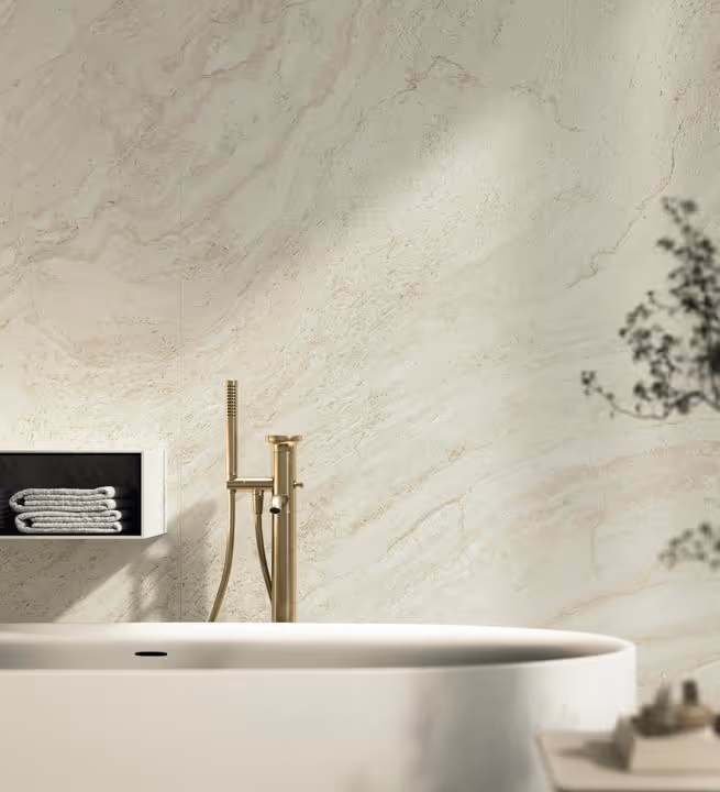 Moderne badkamer met wit vrijstaand bad, gouden kraan en marmeren wand.