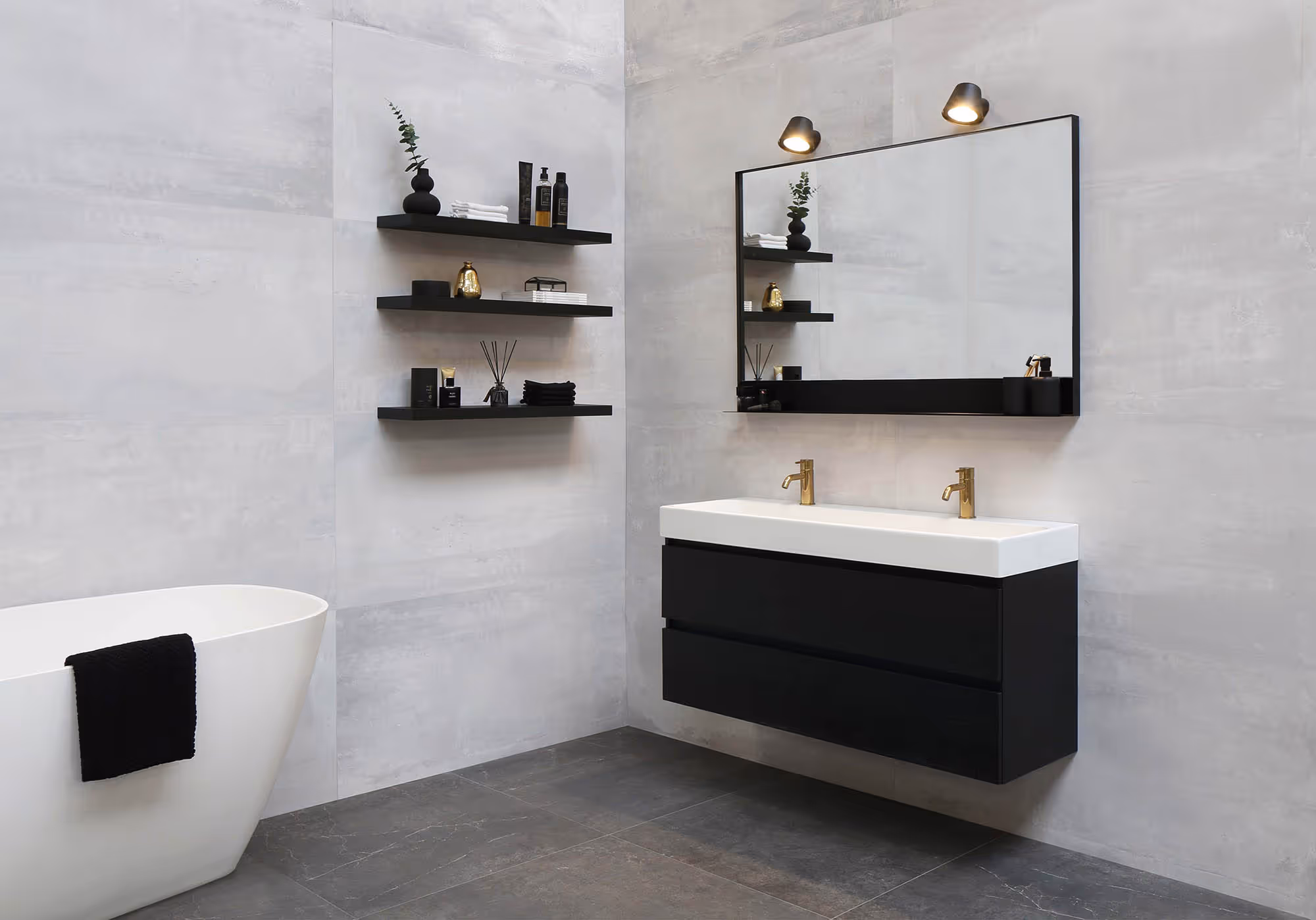 Moderne badkamer met een vrijstaand wit bad met zwarte handdoek, zwevende zwarte wastafel met dubbele gouden kranen, grote spiegel en zwarte wandplanken met accessoires.