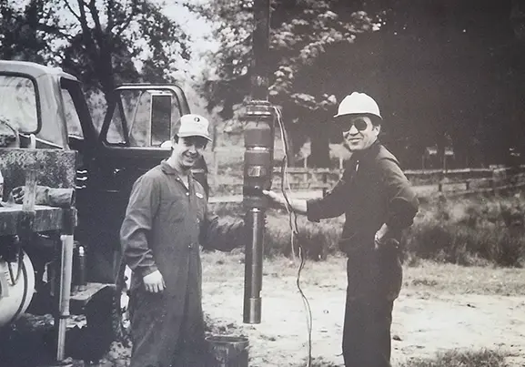 Man wearing brown overalls giving a piggyback ride to a smiling woman in glasses and casual clothes.