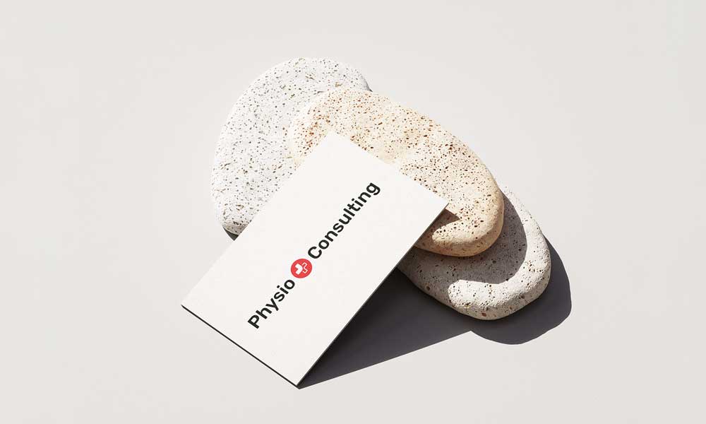 Visitenkarte von Physio Consulting mit rotem Logo auf weissem Karton, drapiert auf natürlichen Steinobjekten