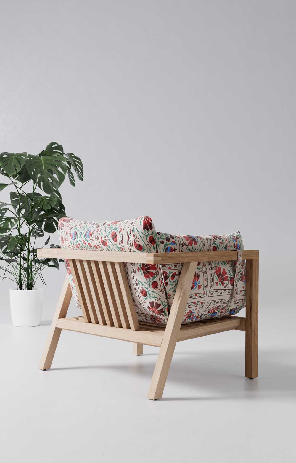 Umomoku Loungesessel mit hellem Holzrahmen und floraler Suzani-Stoffpolsterung in Rot und Weiss, Seitenansicht mit Monstera-Pflanze