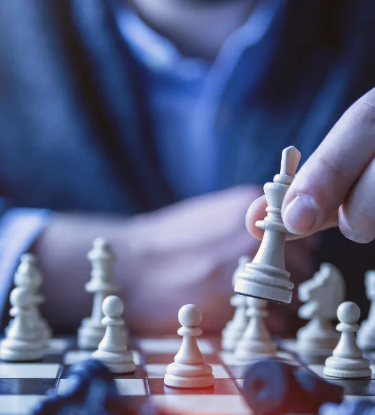 Une personne en tenue professionnelle déplace une pièce blanche sur un échiquier, illustrant la stratégie et la prise de décision.