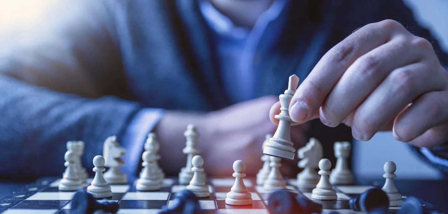 Une personne en tenue professionnelle déplace une pièce blanche sur un échiquier, illustrant la stratégie et la prise de décision.