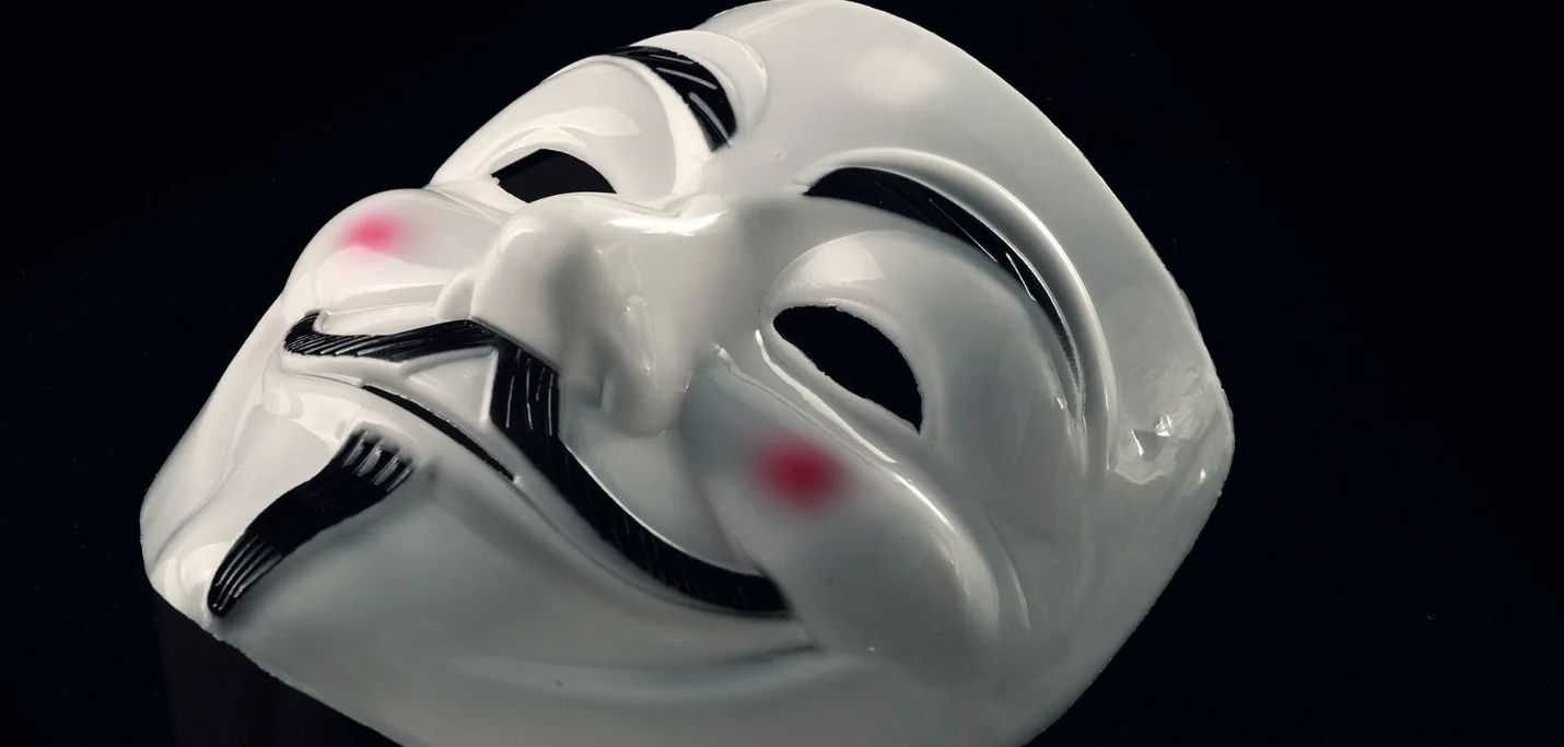 Masque blanc souriant de Guy Fawkes sur fond noir, symbole de l’usurpation d’identité en ingénierie sociale