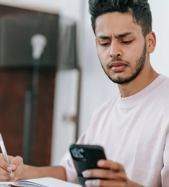 Jeune homme barbu en t-shirt clair, sourcils froncés, qui fixe son smartphone d’un air méfiant devant un message suspect