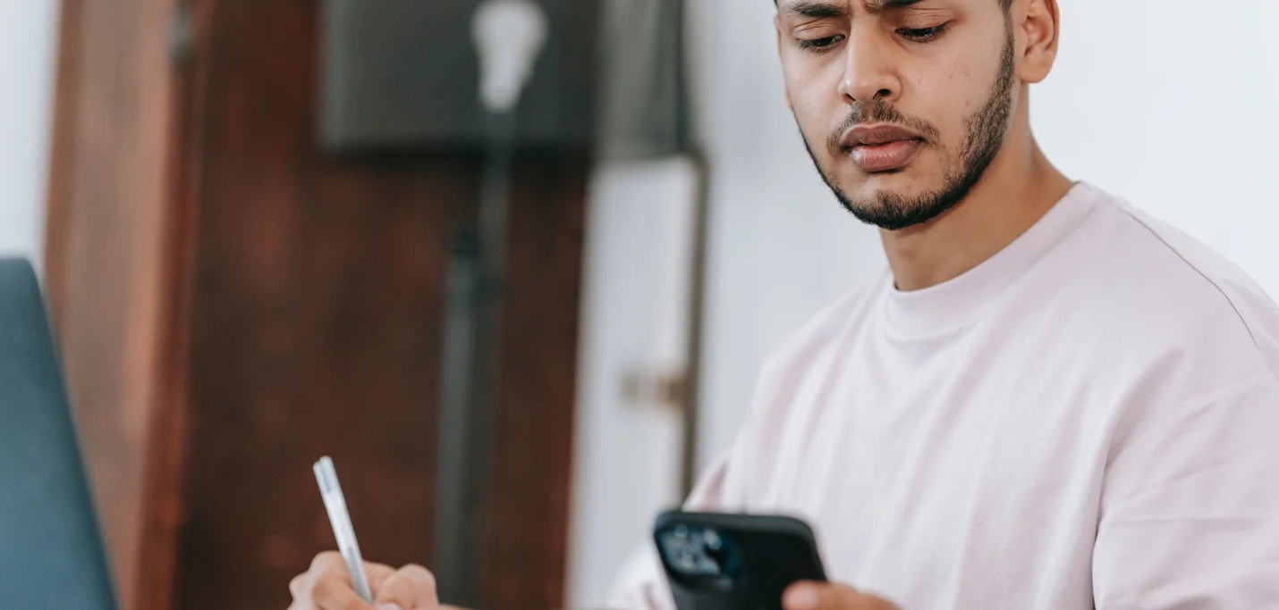 Jeune homme barbu en t-shirt clair, sourcils froncés, qui fixe son smartphone d’un air méfiant devant un message suspect