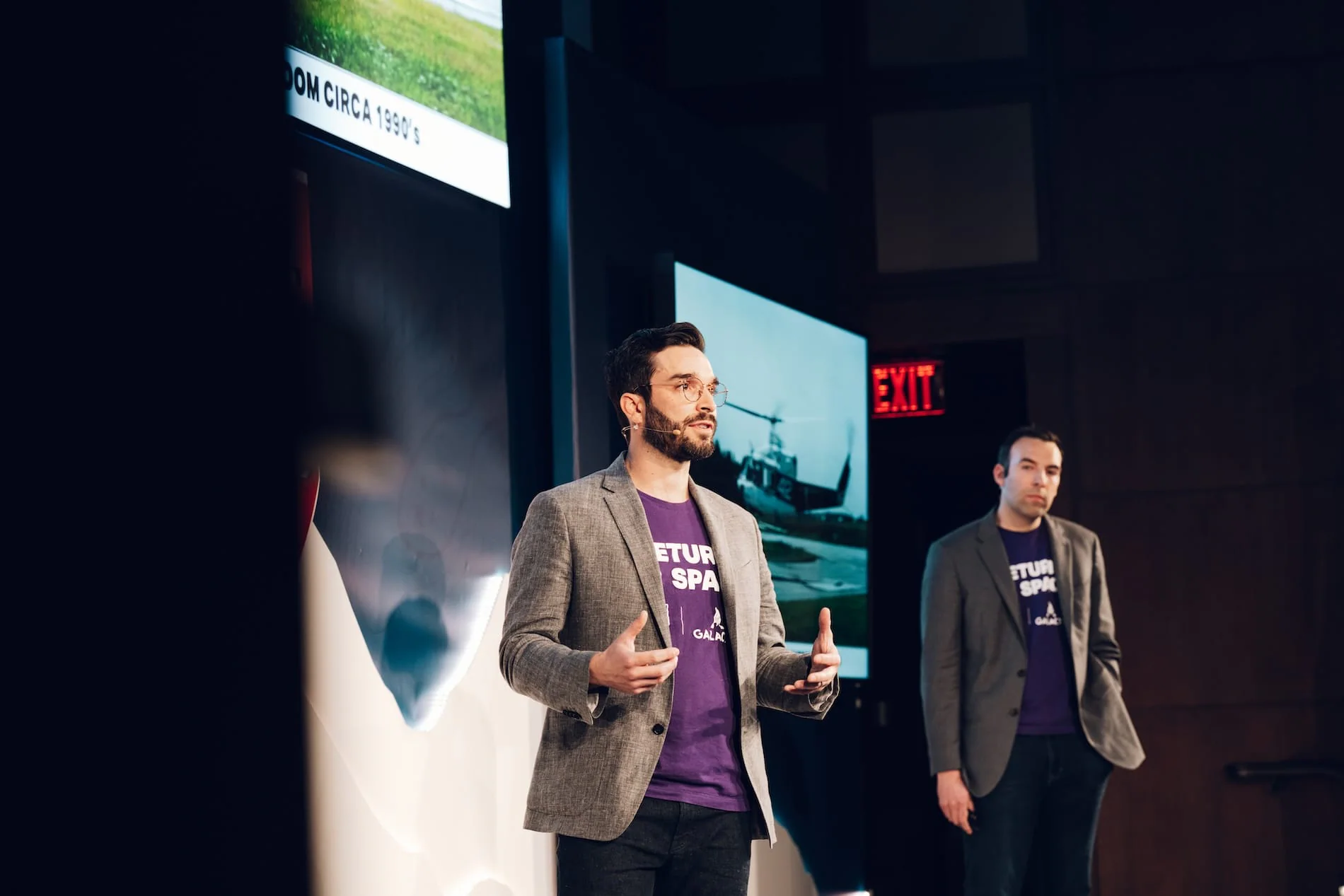 Two presenters on stage, one speaking while wearing a purple "Return to Space" shirt.