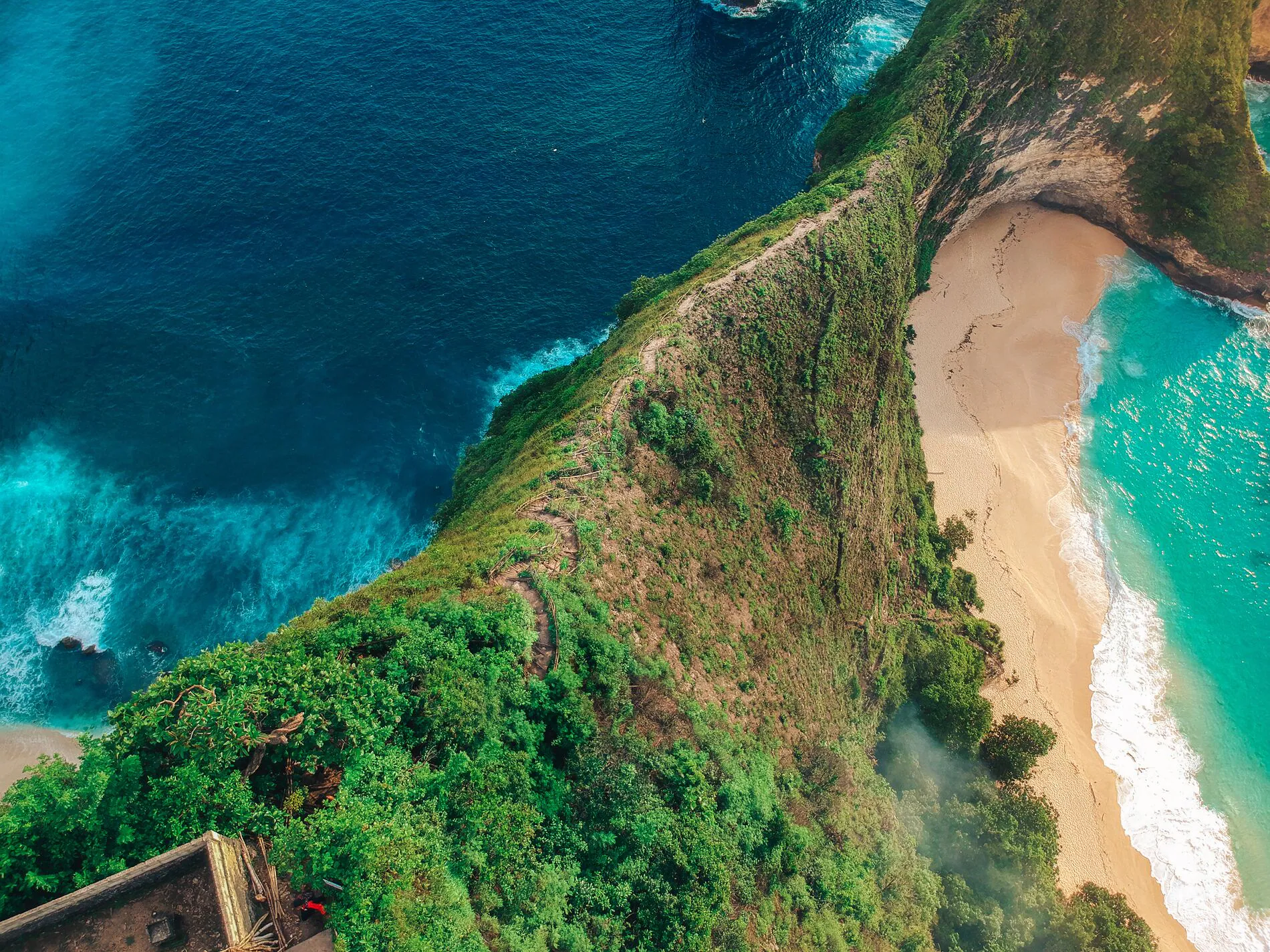 Aerial view of a beach with turquoise water, surrounded by green cliffs and rocky coastline.