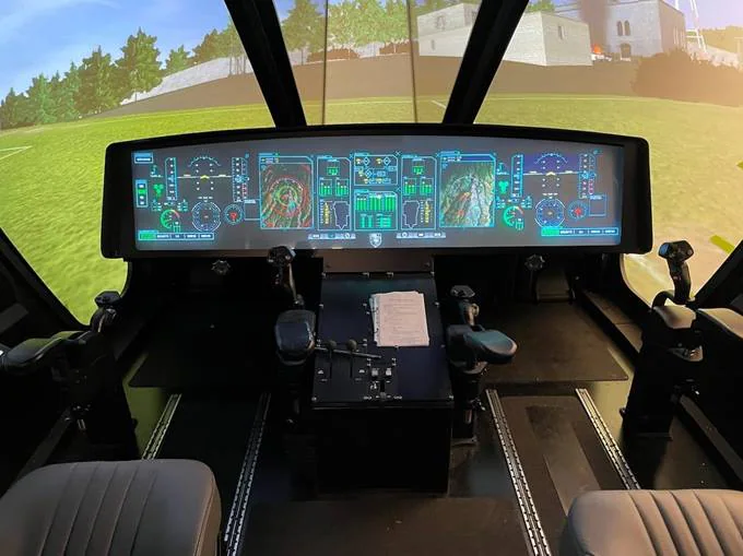 A helicopter cockpit simulator with multiple digital screens displaying various flight instruments.