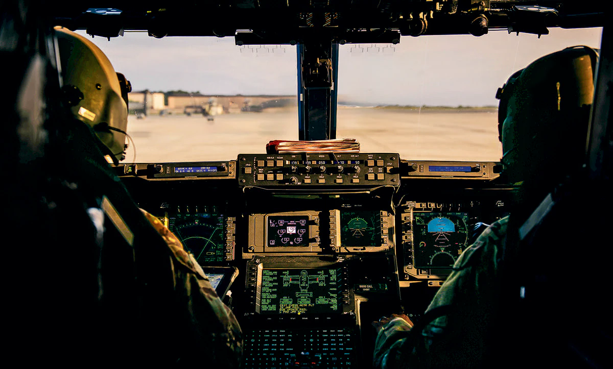 Cockpit view of a military aircraft with two pilots and various control displays.