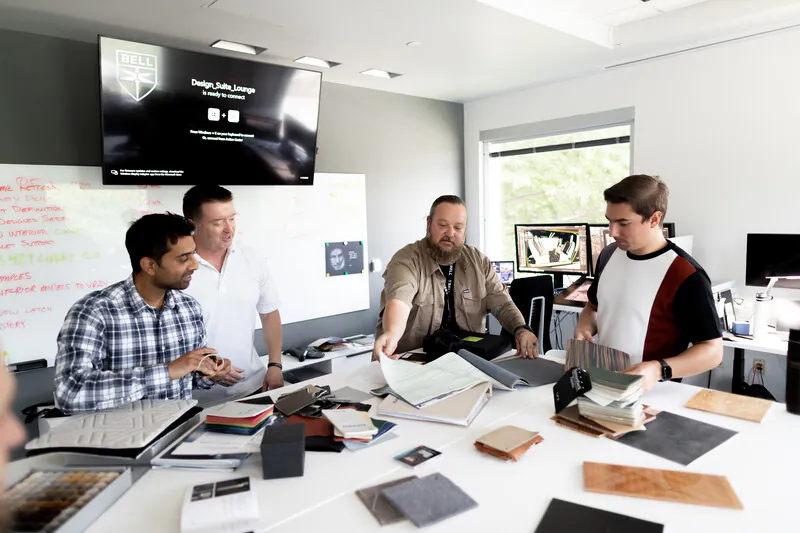 Four individuals collaborate around a table covered with material samples and design documents.