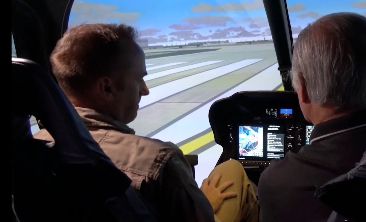 Two pilots in a helicopter simulator, focused on a virtual runway displayed on screens.