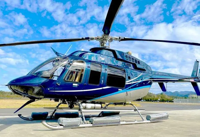 A blue and silver helicopter parked on a tarmac under a cloudy blue sky.