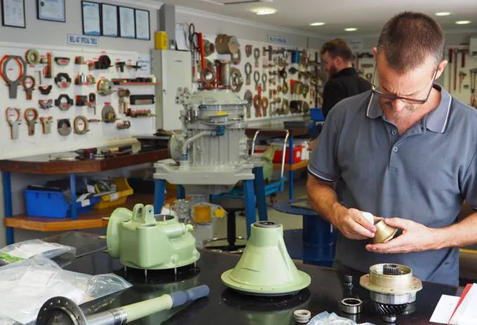 A technician inspects engine parts in a workshop filled with tools and equipment.