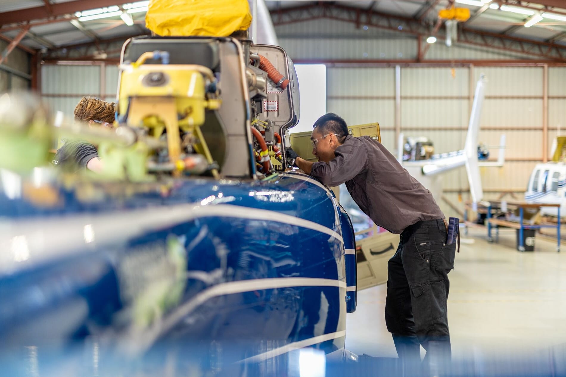 Mechanic inspecting the cockpit of a blue aircraft in a hangar. Tools and equipment visible.