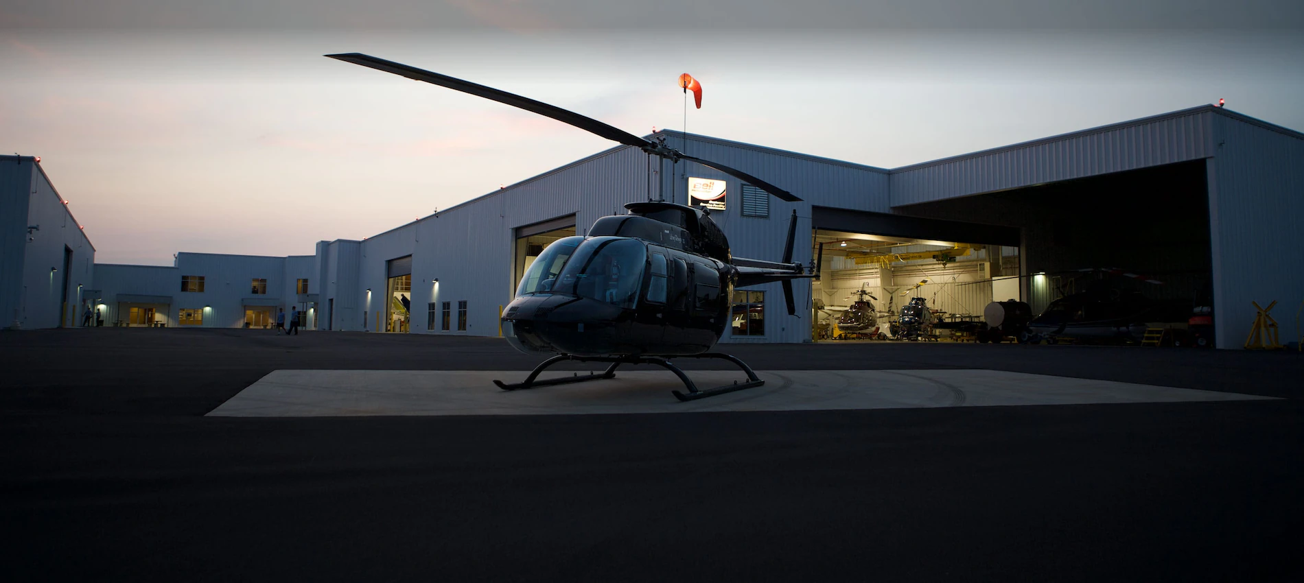 Helicopter parked on a helipad in front of a hangar at dusk.