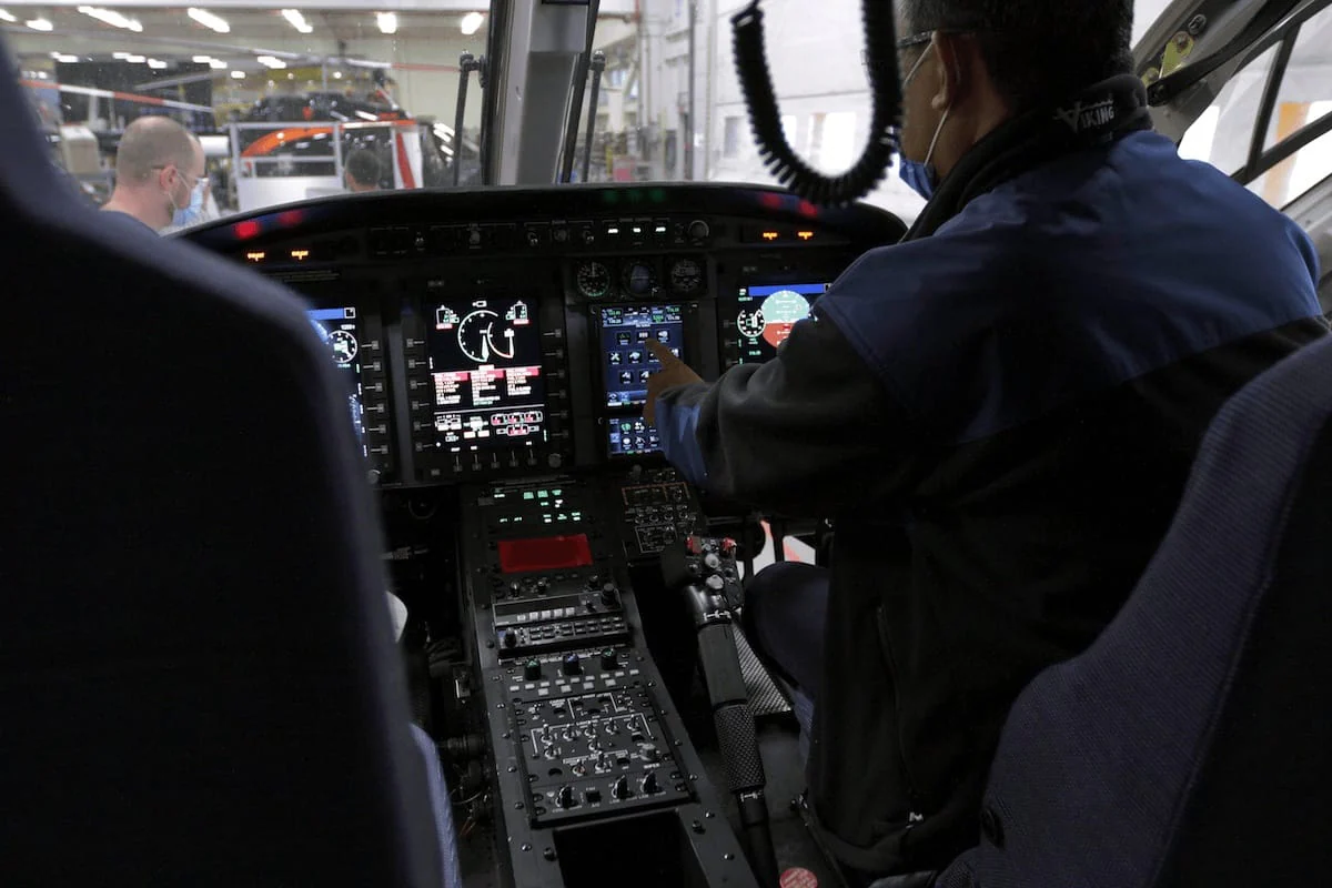 Cockpit view of a helicopter showing controls and displays, with a pilot adjusting settings.