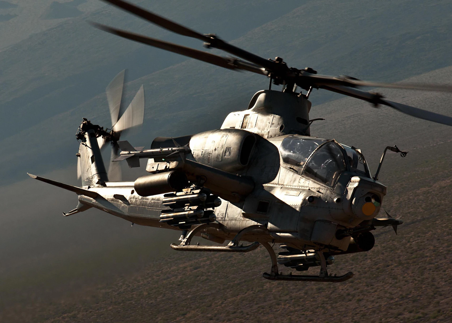 A military helicopter flying over a mountainous landscape with visible weaponry.