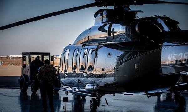 Black helicopter parked in a hangar with a person preparing to board and a service vehicle nearby.