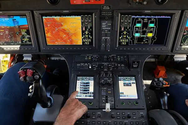 Cockpit view with multiple monitors displaying flight data and controls for aircraft operation.